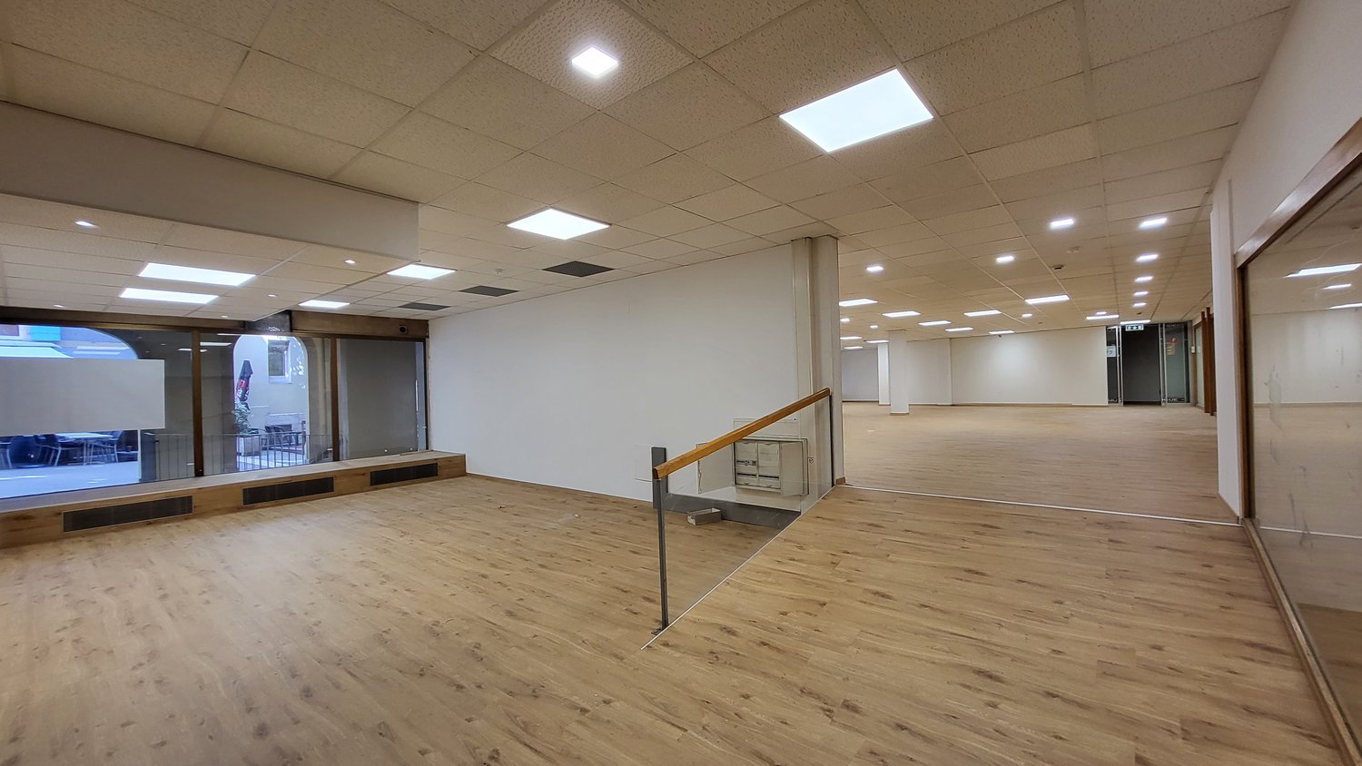 wooden floor, white walls, ceiling with fluorescent lights, windows, glass doors