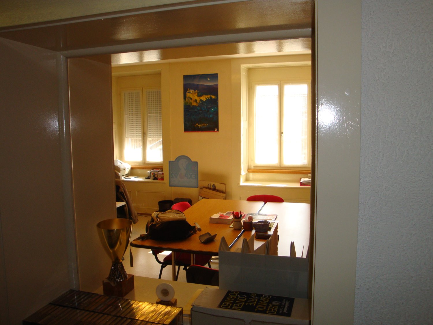 A room with a desk, chairs, a trophy, a poster, and a window.