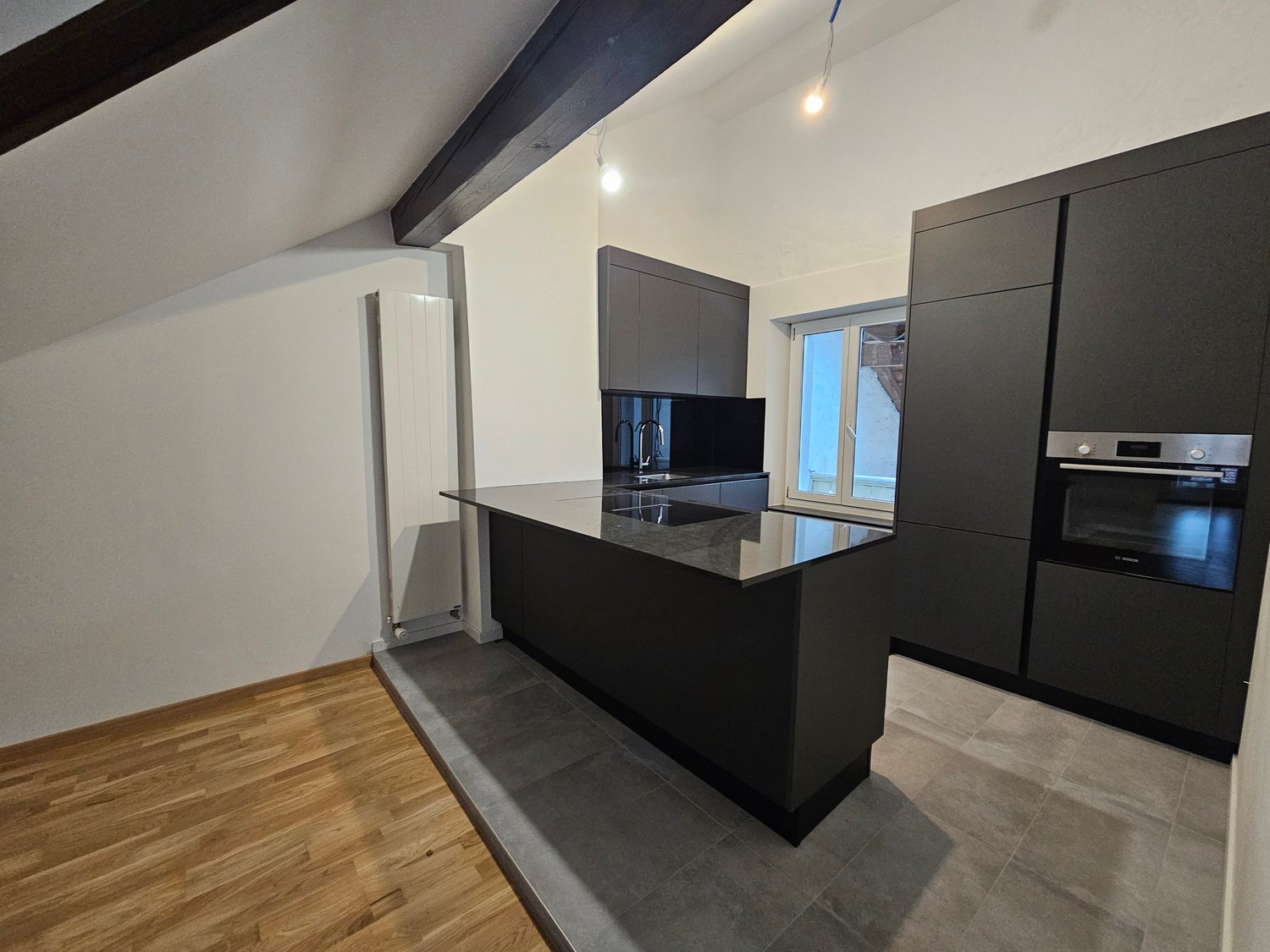 Island with sink, modern appliances, black cabinetry, tiled flooring, large windows