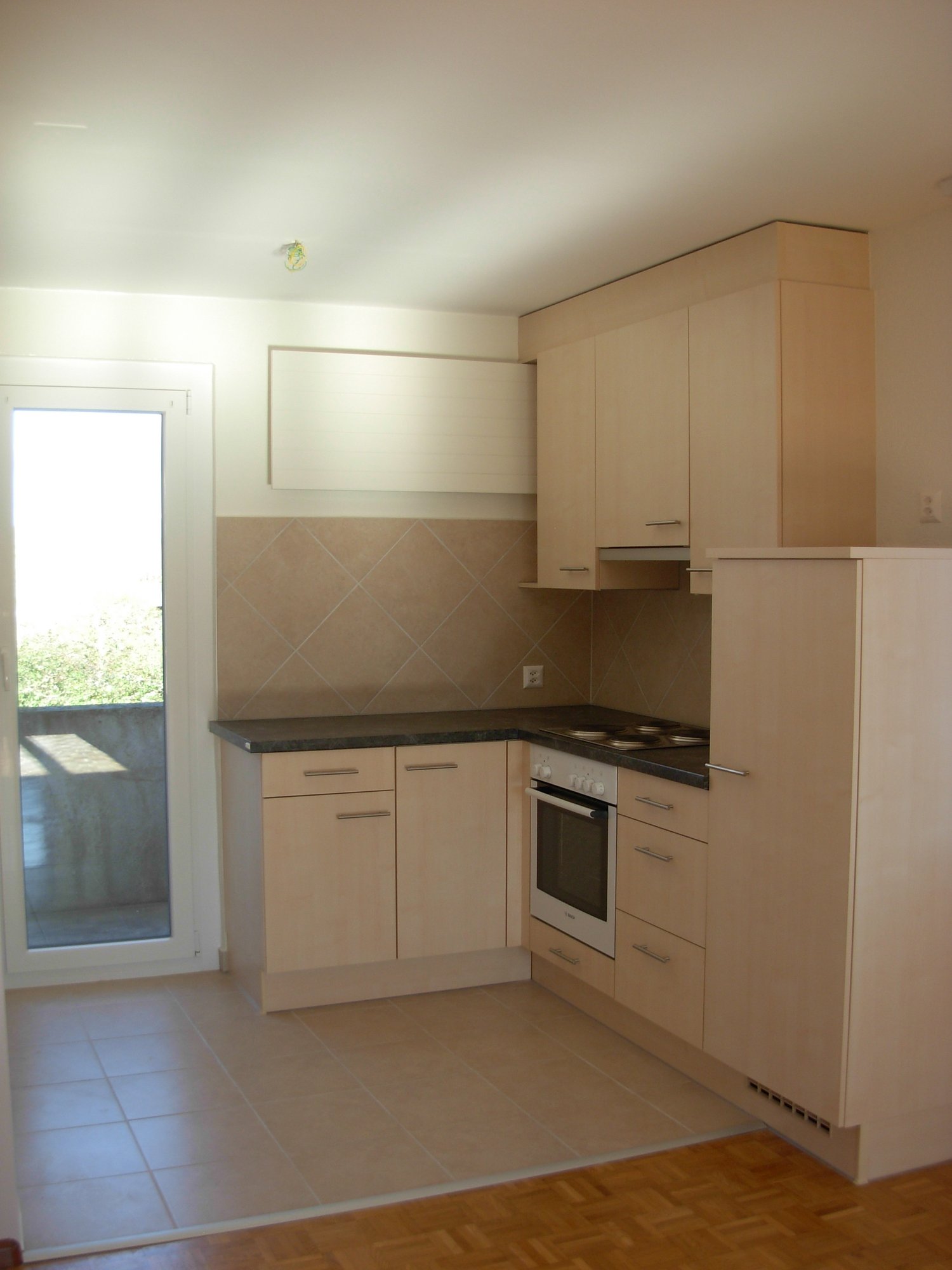 modern kitchen with wooden cabinets, granite countertop, electric stove, oven, and a sliding door leading to a balcony