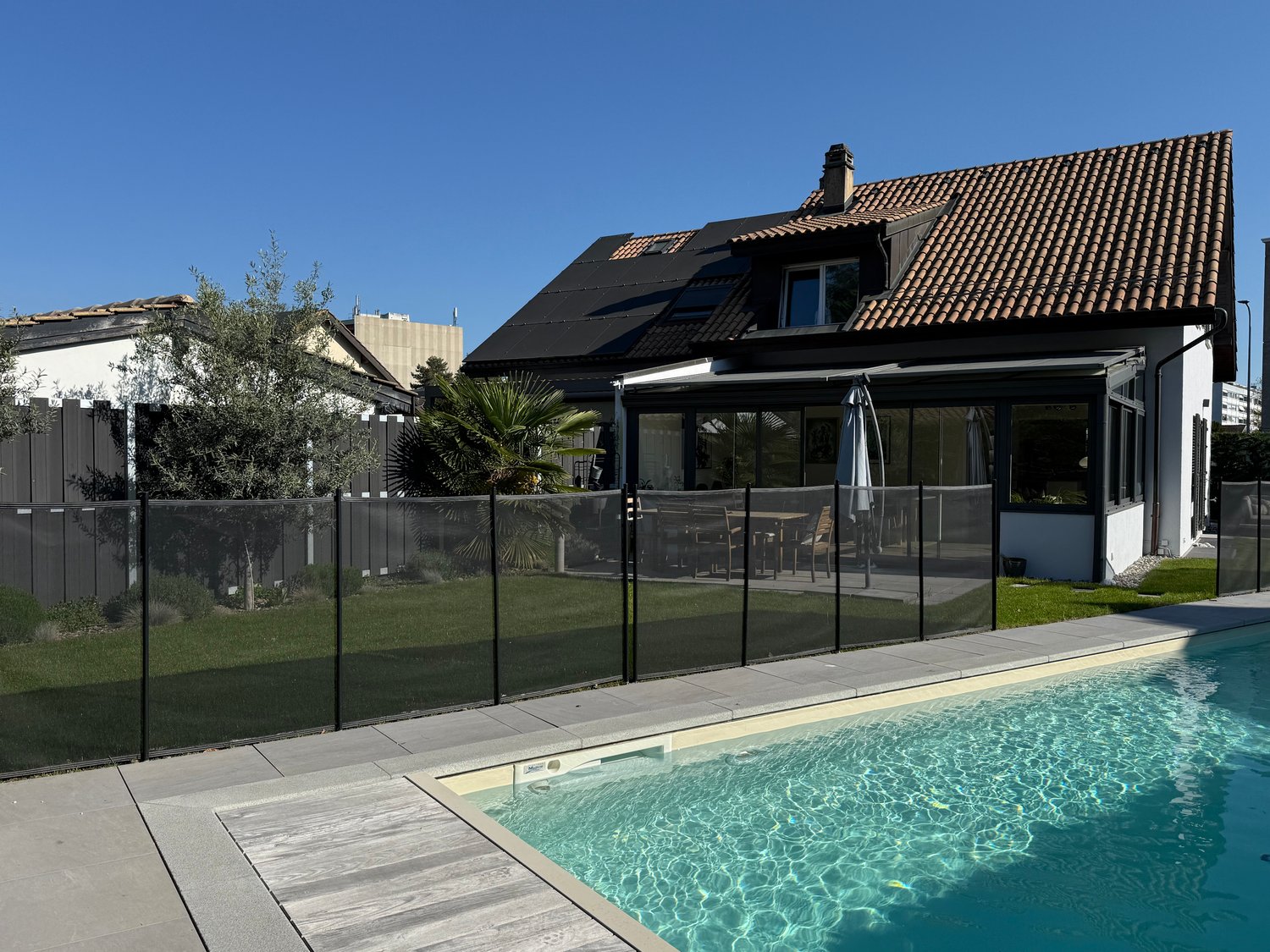 Modern house with brown roof, glass windows, black fence, swimming pool, wooden deck