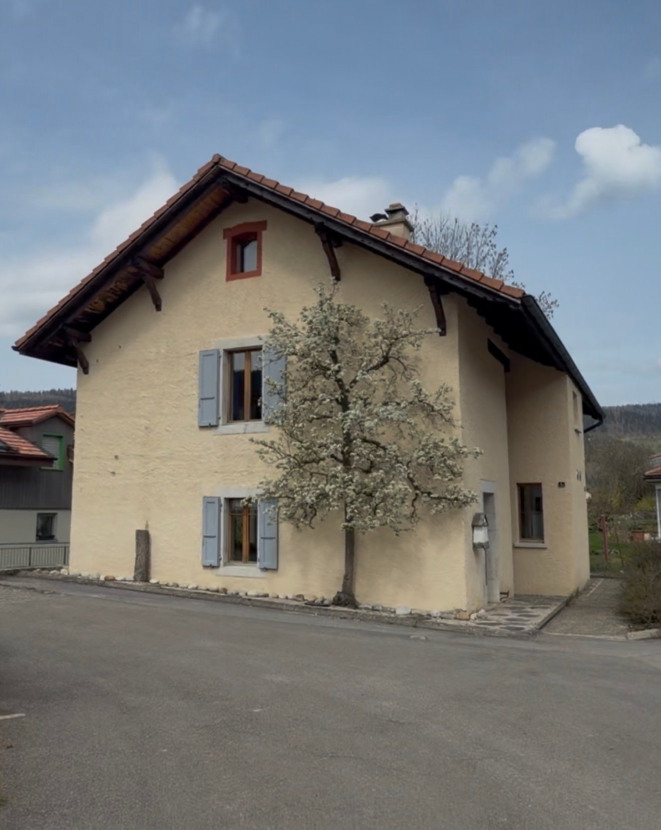 2 story house, beige walls, brown roof, windows with shutters, tree in front