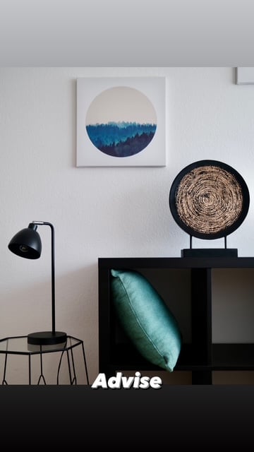 Furnished Room. A modern, minimalist room with a sleek black table, a teal cushioned chair, a contemporary floor lamp, a woven decorative sculpture, and a large abstract painting on the wall.