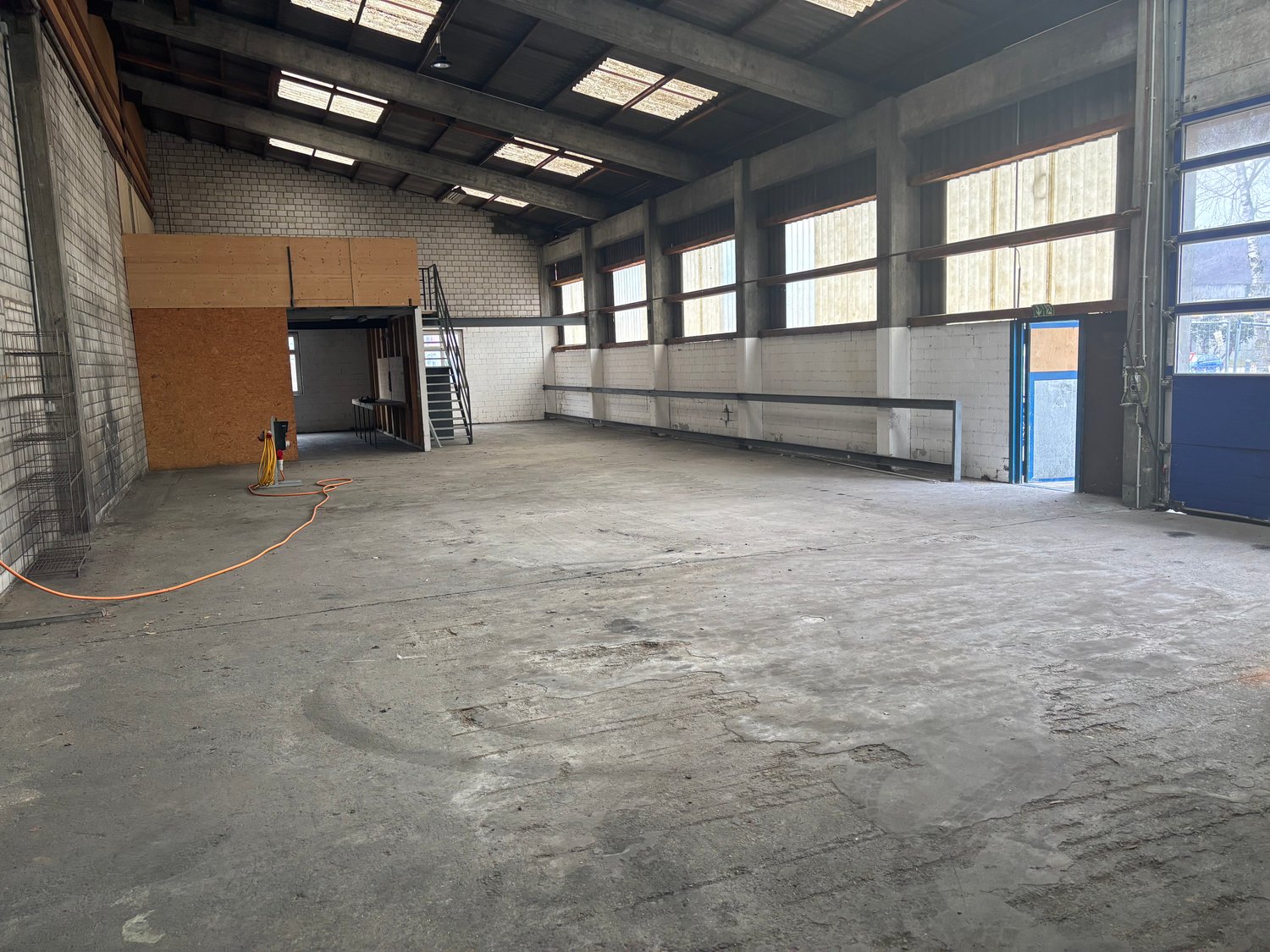empty warehouse with concrete floor, large windows, metal ceiling beams, side doors