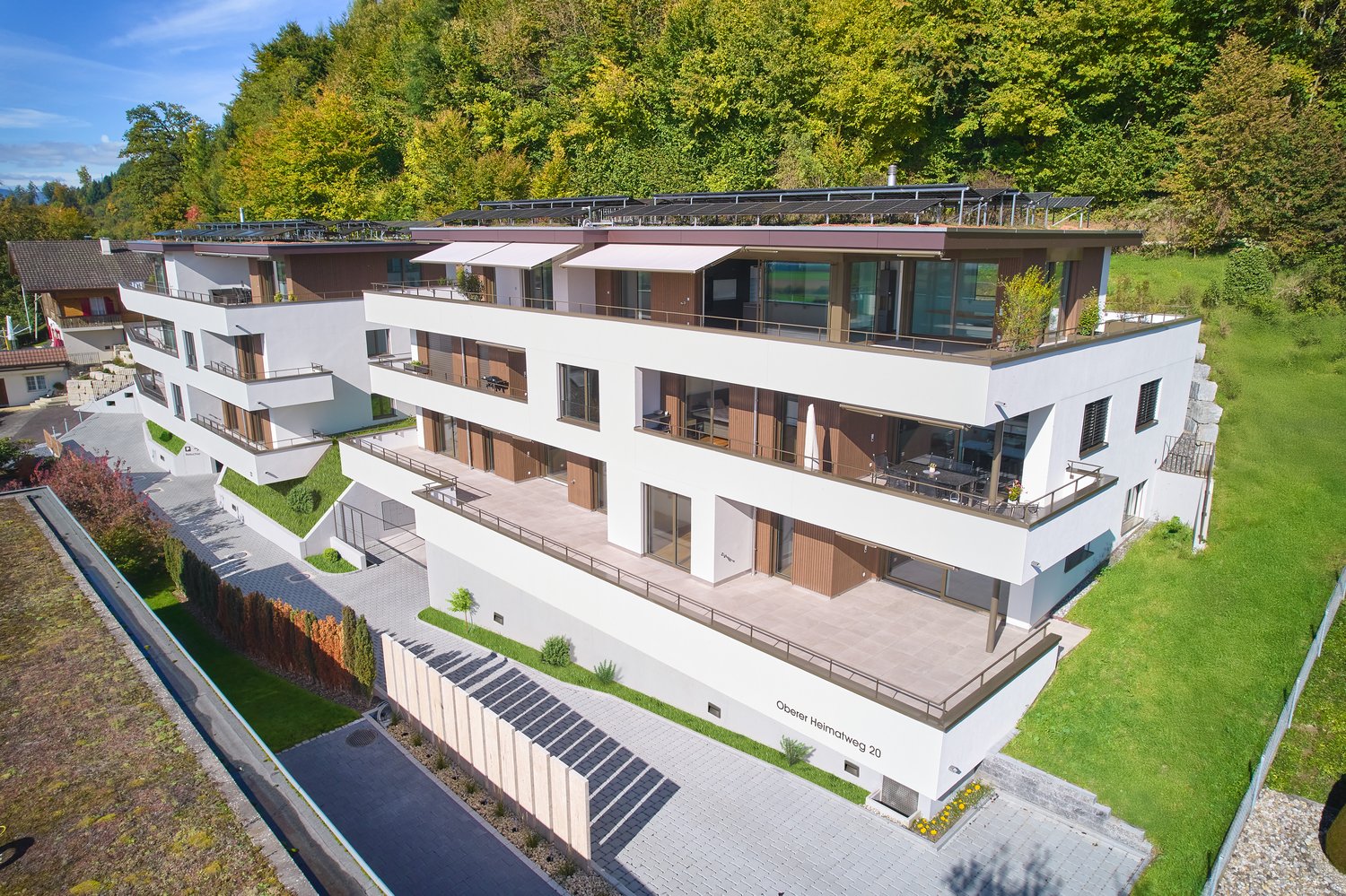 Two-story apartment building with solar panels, white exterior, balconies, terraces, and a driveway