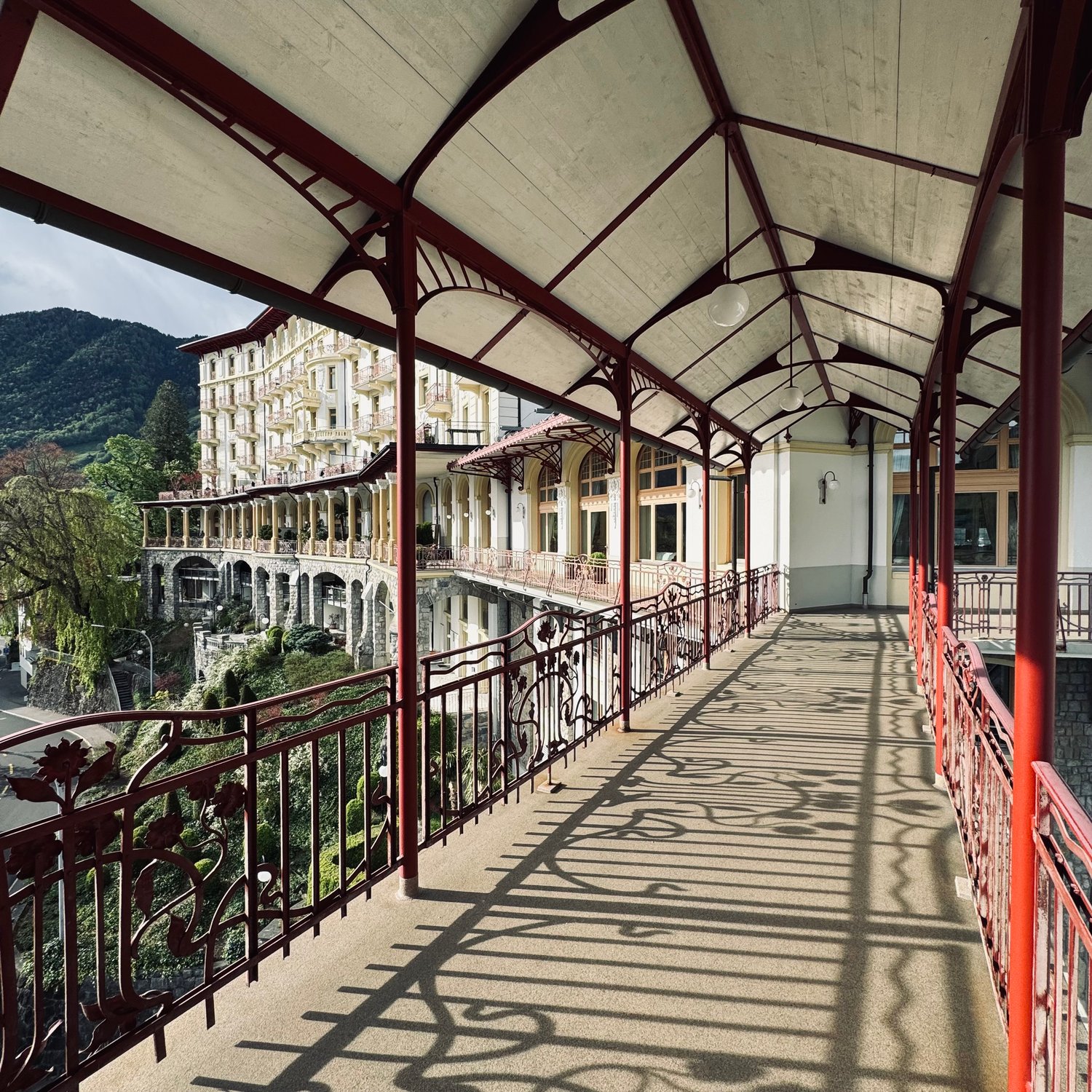 This image shows a historic building with a covered walkway or balcony. The building has a distinctive architectural style with arched windows and ornate railings. The walkway is supported by metal beams and has a slanted roof. The building appears to be
