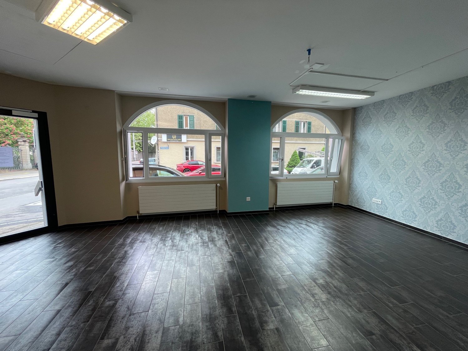 an empty room with hardwood floors, arched windows, ceiling lights, and two white radiators on the wall