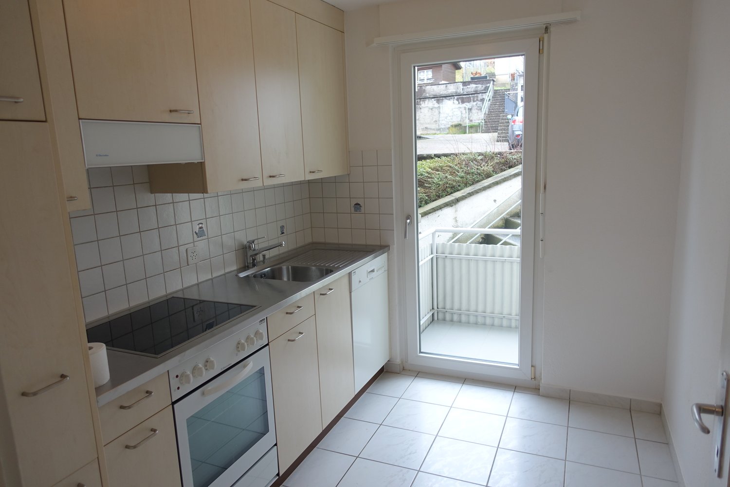 Spacious kitchen with white cabinets, tiled backsplash, stainless steel sink, and a glass door leading to a balcony or terrace area.