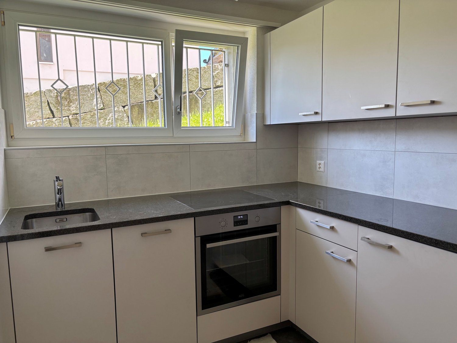 Modern kitchen with white cabinets, stainless steel sink, and built-in oven. Features grey countertops and tiled backsplash.
