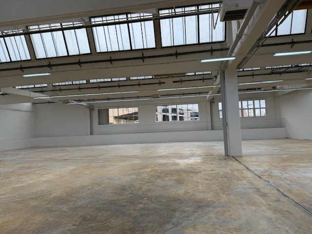 large empty room, high ceiling, concrete floor, many windows, metal ceiling beams
