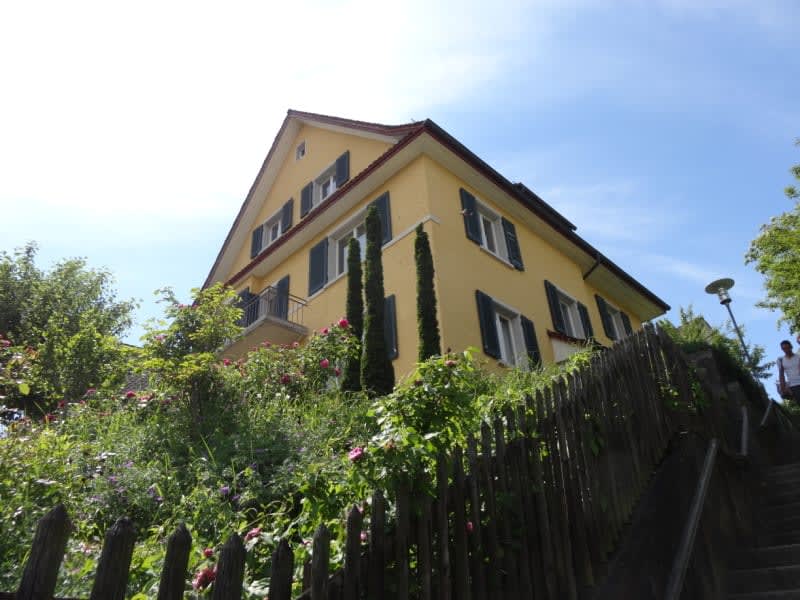 2 story yellow house, raised ground floor, balcony, brown roof