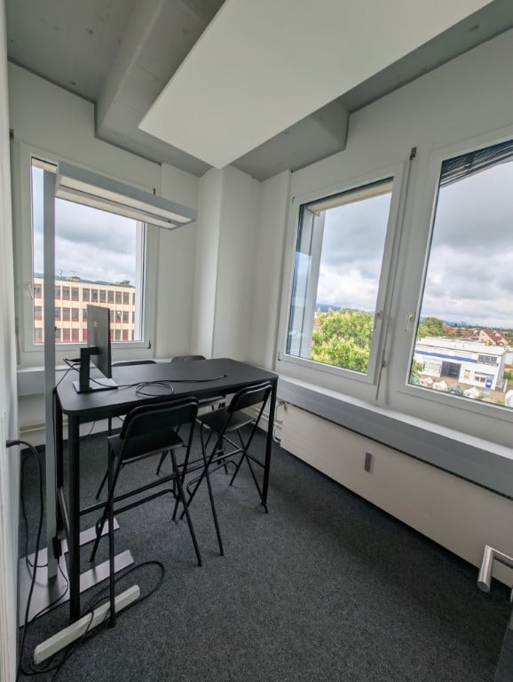 Spacious office room with large windows providing a view, black desk and chairs, carpeted floor