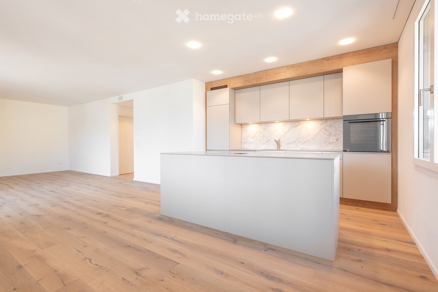 Modern kitchen with light-colored cabinets, a white kitchen island, and a built-in oven. The space features wooden flooring and recessed lighting.