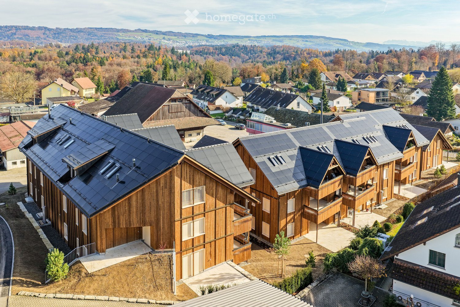 Aerial view of several wooden houses with solar panels on roofs, surrounded by nature with trees and mountains