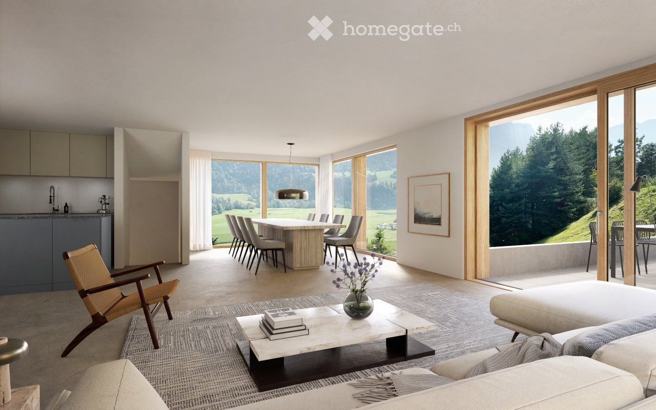 Spacious open-plan living room with large windows offering a scenic view of the surrounding countryside. The room features a dining area with a wooden table and chairs, a comfortable seating area with a sofa and armchair, and a modern kitchen with gray ca