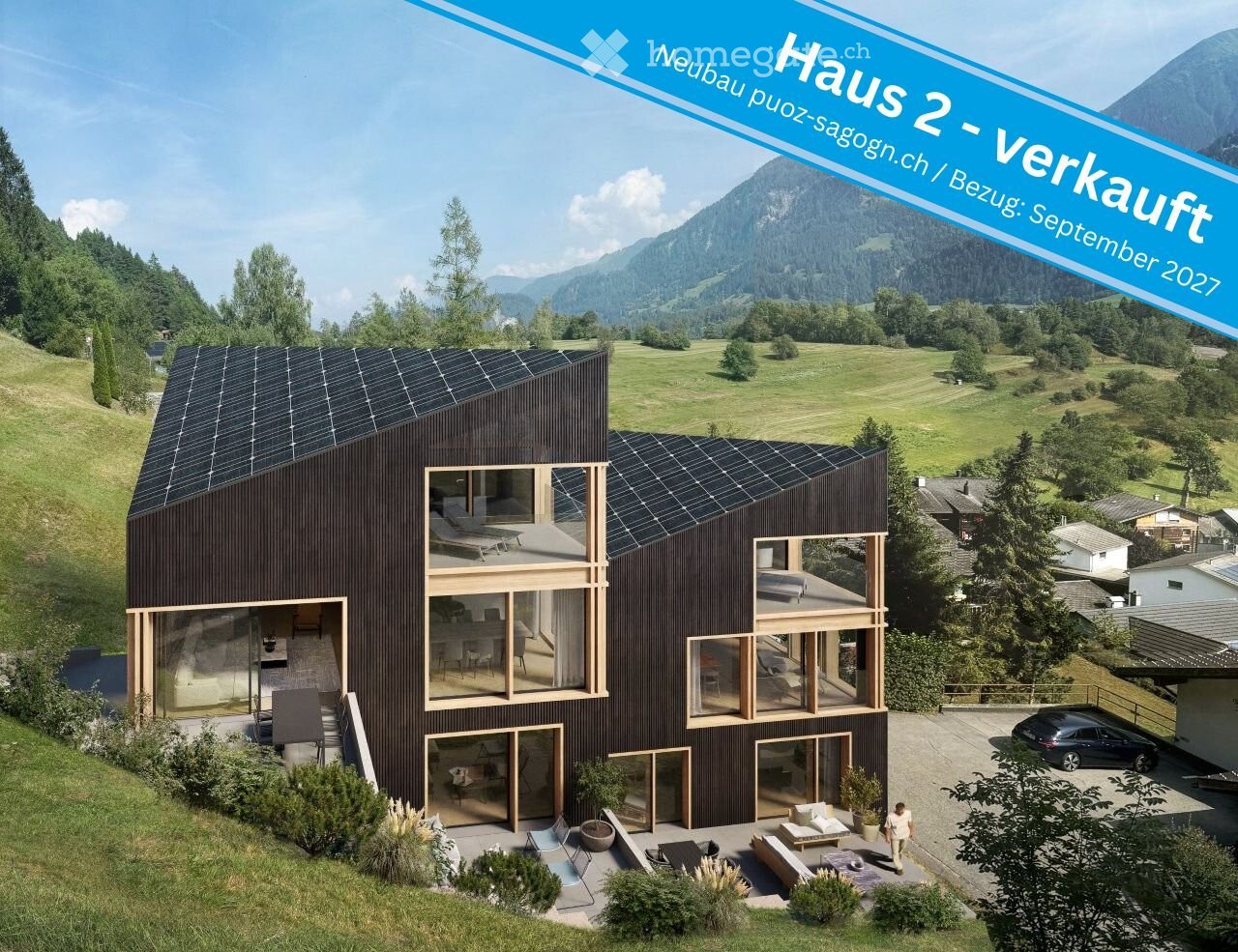 Modern two-story house with dark wooden exterior, large windows, solar panels on the roof, and a spacious outdoor patio area with seating.