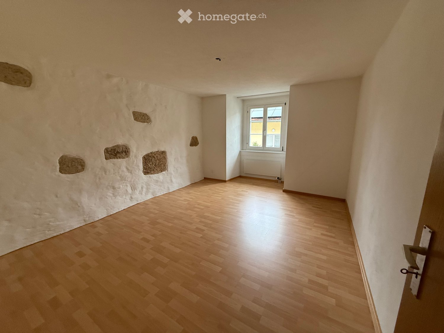 Hardwood floor, wall with exposed stones, white wall, window, radiator, open door