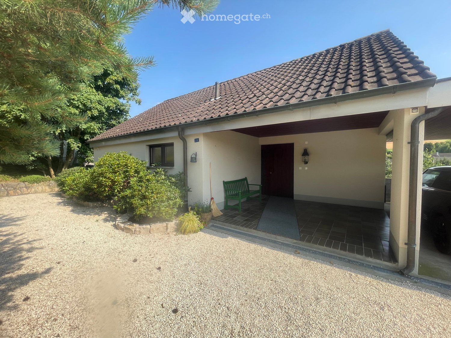 One story house with a brown roof, beige wall, green bench on the entrance, broom, car parked on the garage