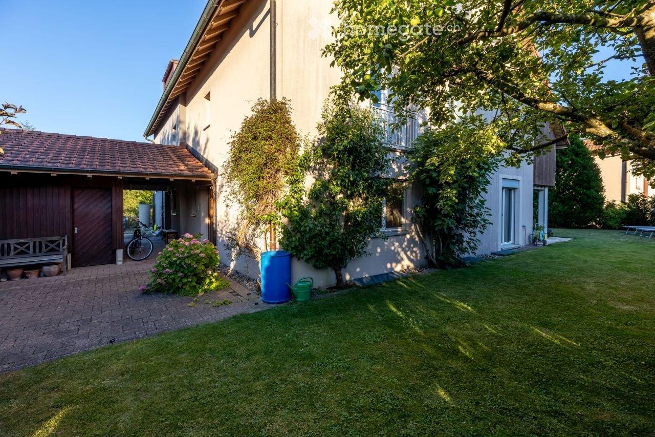 Detached house, brown wooden garage door, well-kept garden with lawn, bicycle and plants
