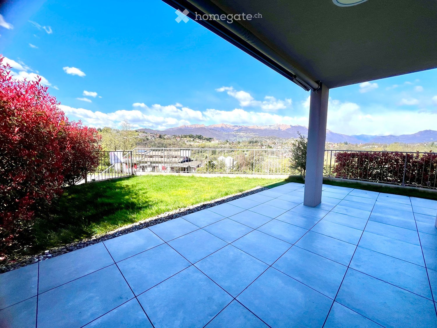 Outdoor terrace with tiled flooring, metal railings, and a view of a grassy lawn and mountains