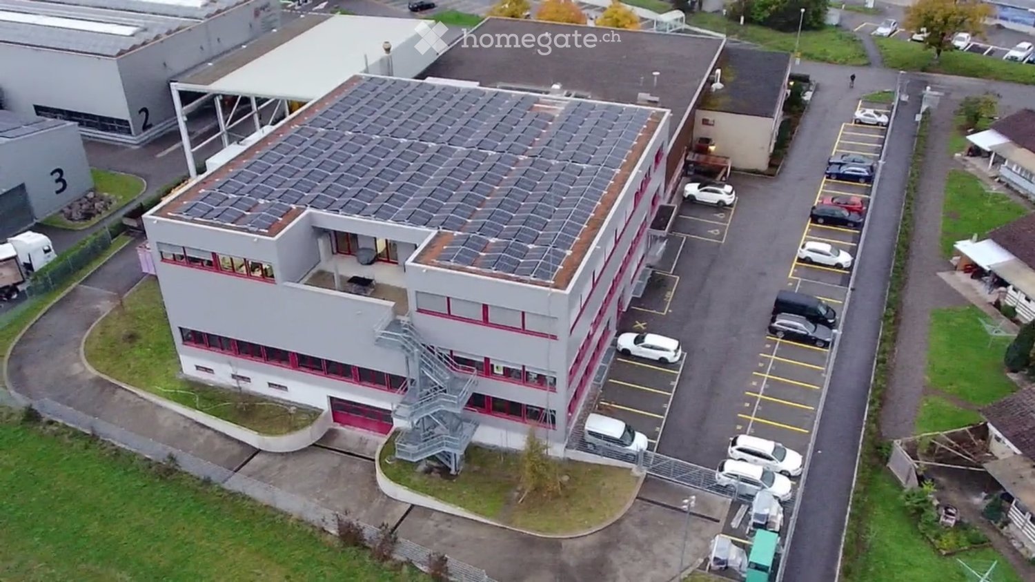 Office building, large roof solar panels, multiple car parking, outdoor staircase, multiple buildings behind
