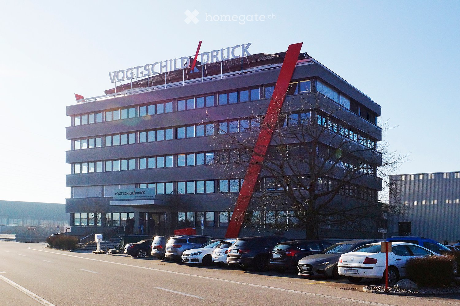 5 story office building with signage 'VOGTSCHILD/DRUCK', several cars parked in front