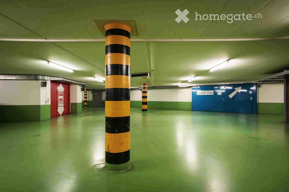 An empty parking area, colored in green, with pillars painted in black and yellow, and some lights attached to the ceiling