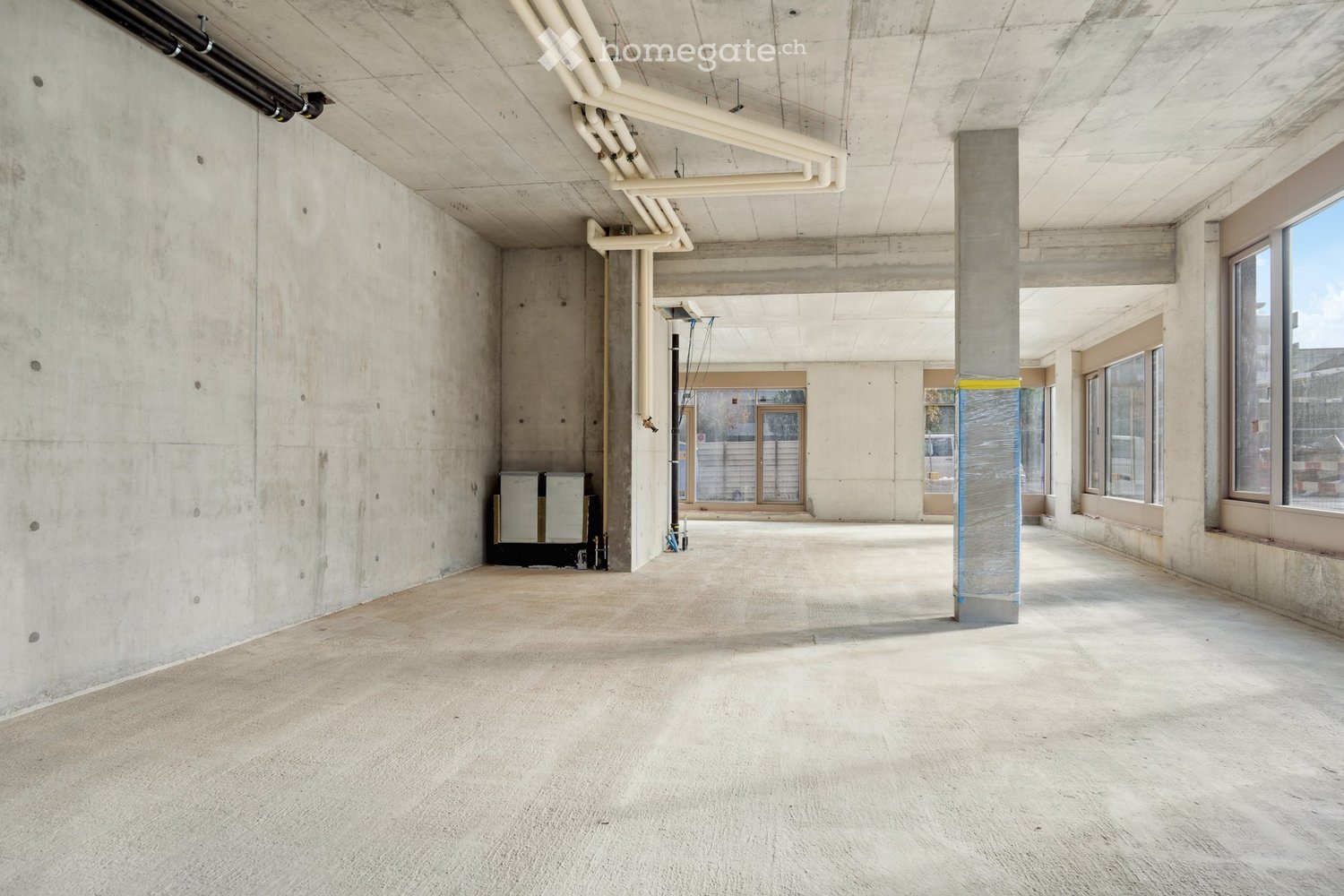 empty room, concrete walls, large windows, central pillar, piping in ceiling