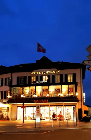 Three story building, illuminated windows, restaurant with visible menu, flag on the roof, Swiss flag