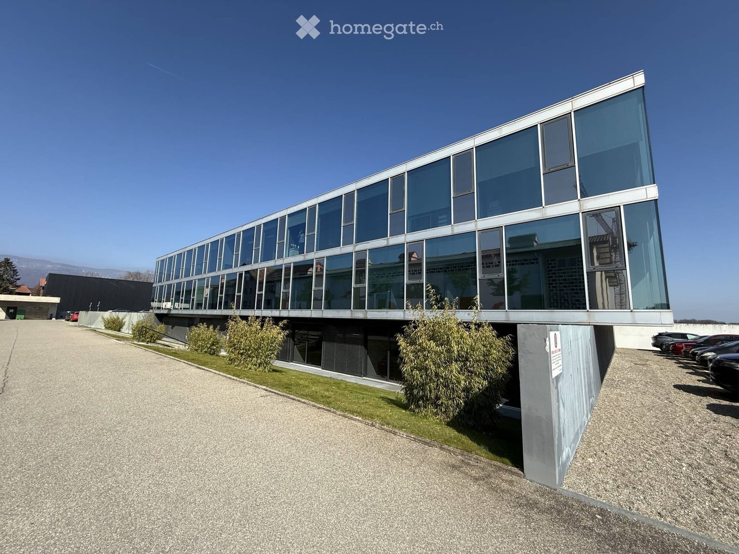 Modern office building with glass walls, concrete wall, parking lot, plants