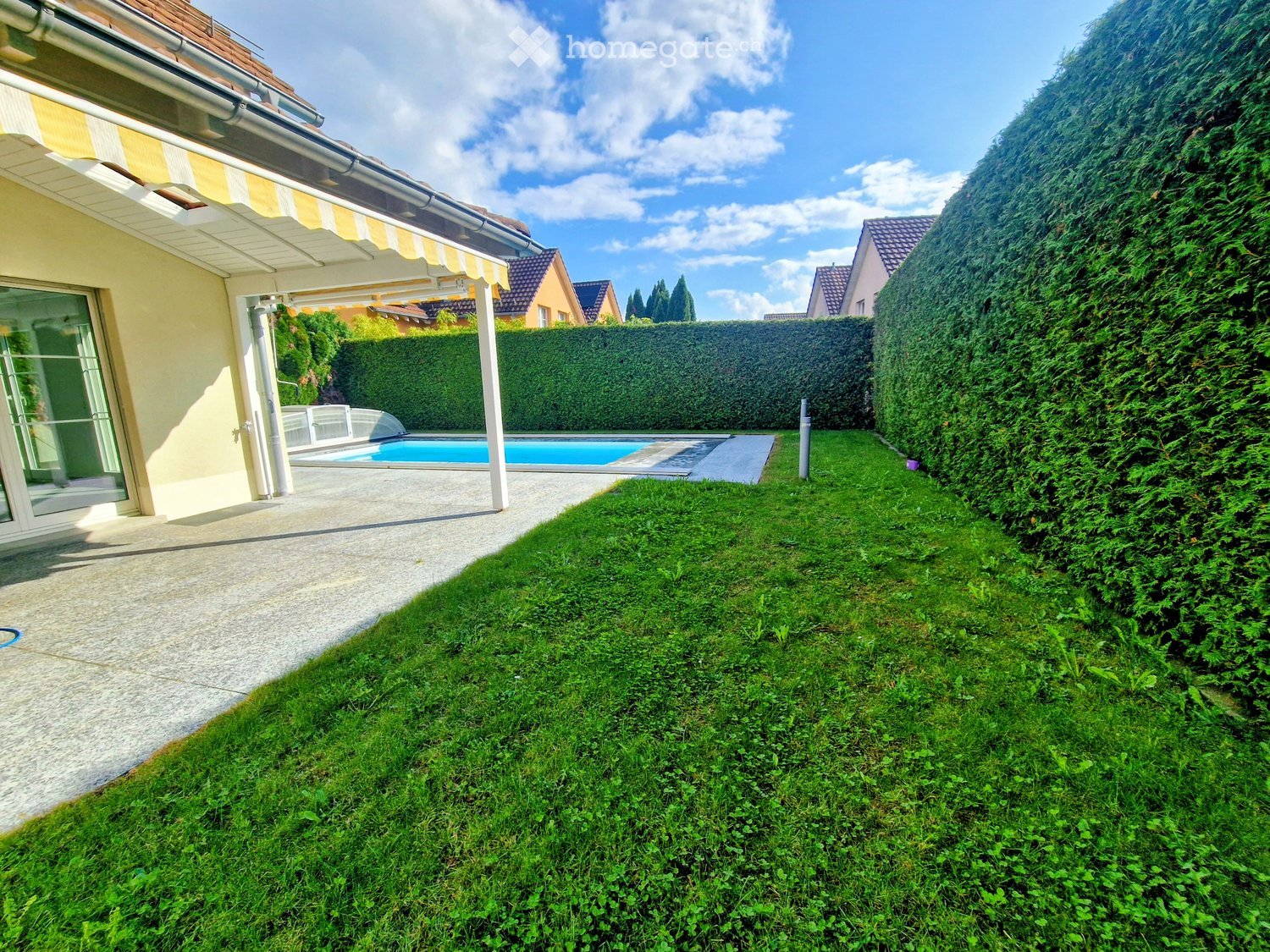 green grass, raised ground, swimming pool, terrace with awning, lawn and bushes