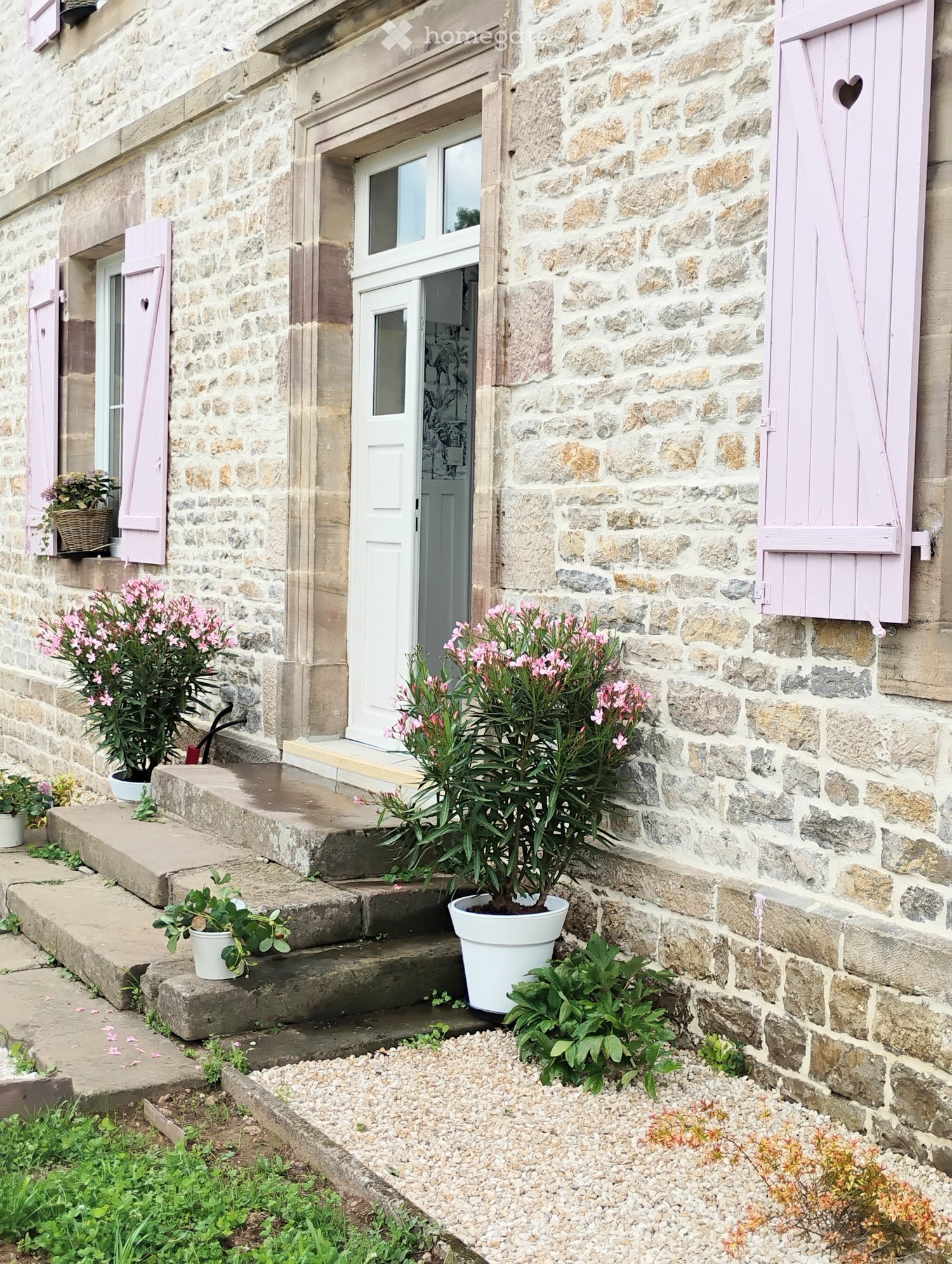Stone exterior, pink shutters, white front door, potted flowers at the front steps