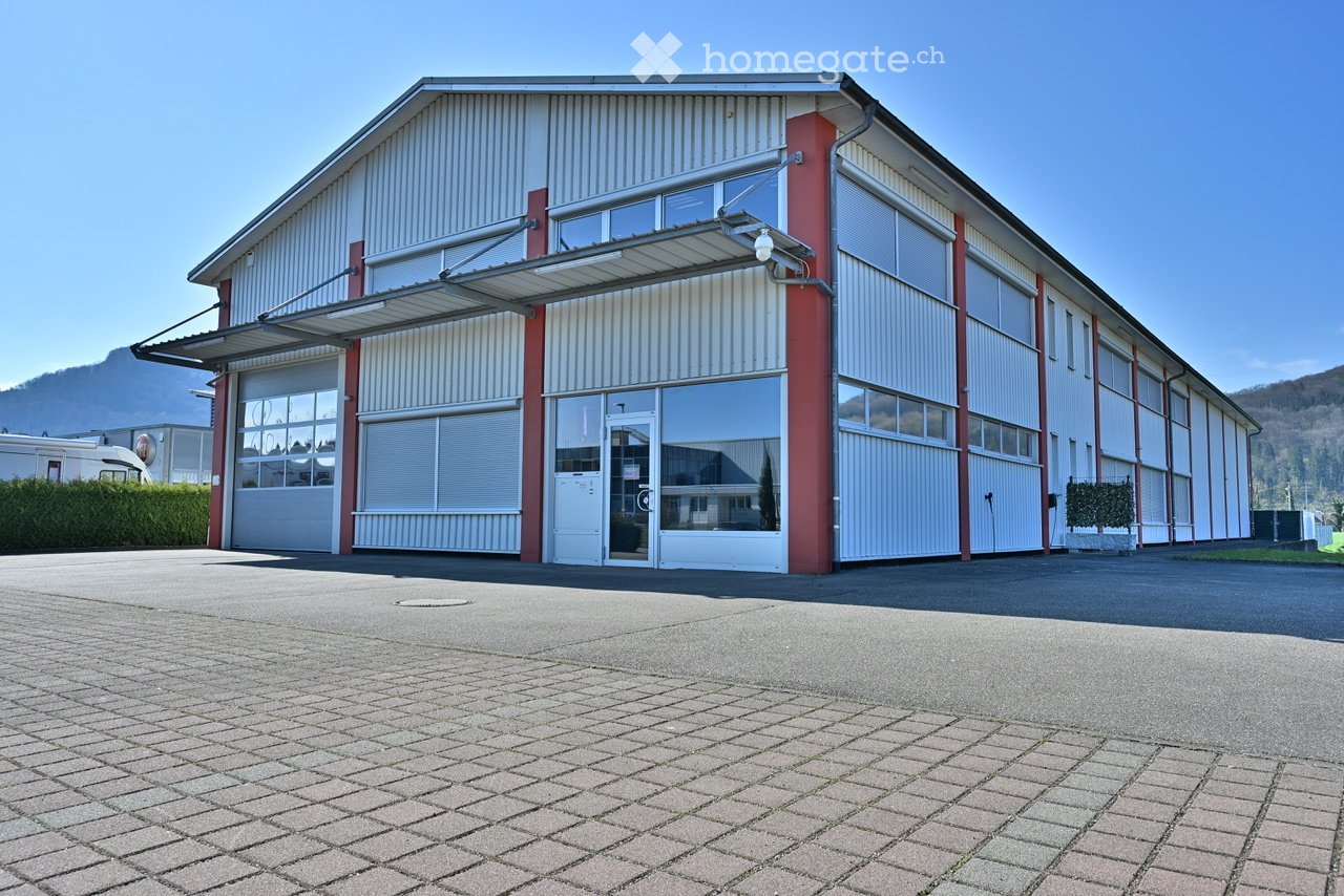 Warehouse-style building, large windows, roll-up doors, red trim, parking area