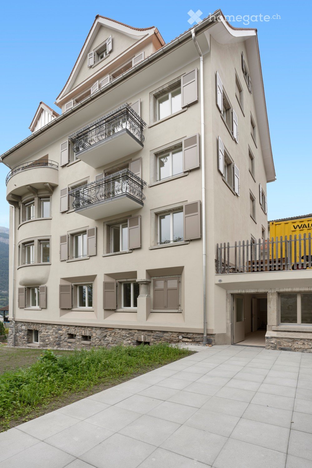 large apartment building, beige facade, several balconies, stone base, garage entrance