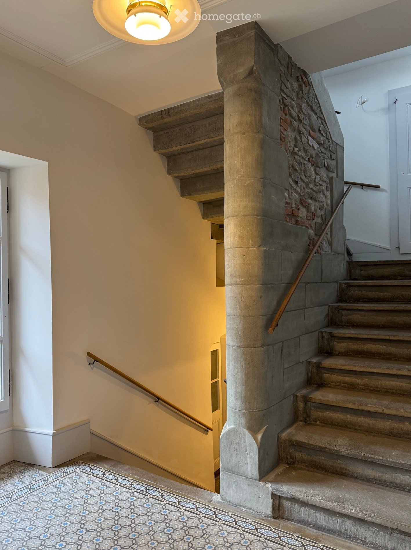 interior staircase with patterned tile flooring, cement pillar, wooden handrail, white walls, natural light