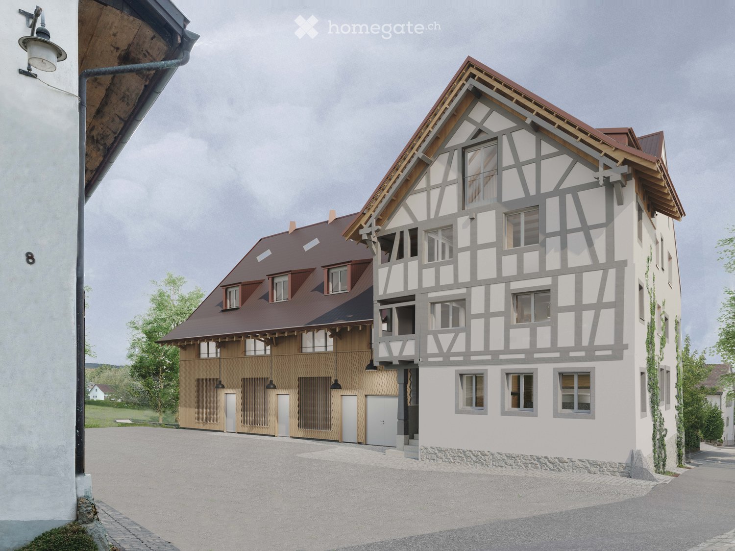 Two-story building with a half-timbered facade, red-tiled roof, and garages on the ground floor. The building has a traditional German architectural style.