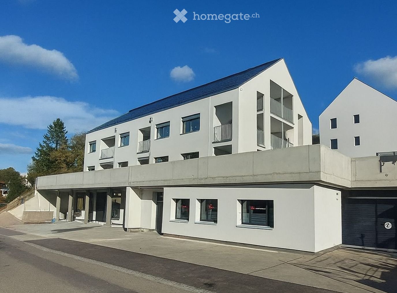 modern white building, raised ground floor, multiple balconies, garage entrance, solar panels on roof, ground level windows, street view