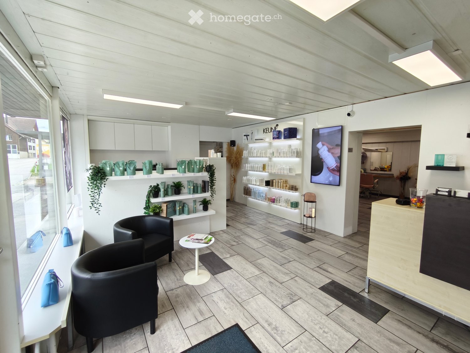 modern office space with white walls, gray floors, large windows, white shelves, black chairs, small white table, large black monitor mounted on wall