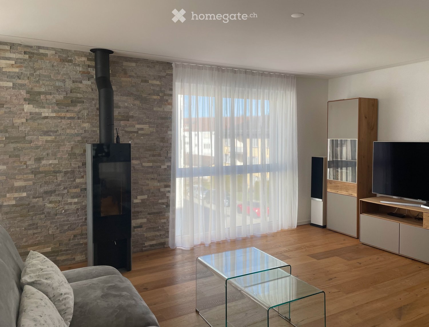 living room, fireplace, large window, couch, glass coffee table, speakers, television, wooden floor