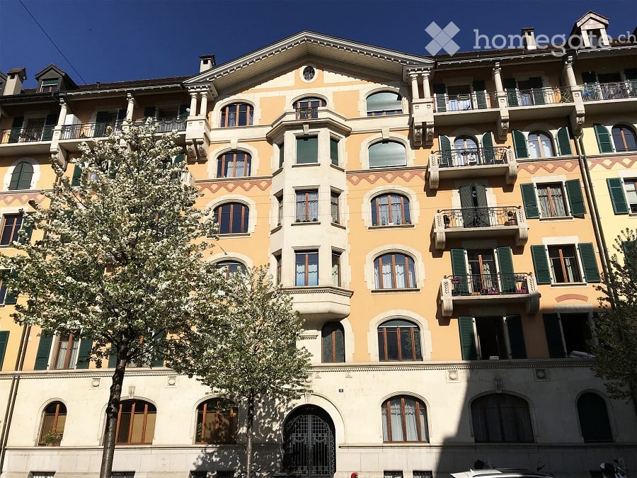 6-story building, beige and brown facade, balconies, windows with shutters, tree in front