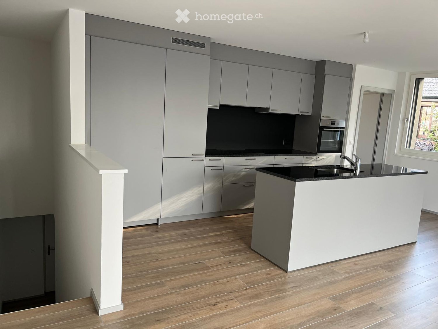 modern open-plan kitchen with island, black countertop, wooden floors, gray cabinetry, black backsplash, stainless steel sink, modern appliances, central lighting