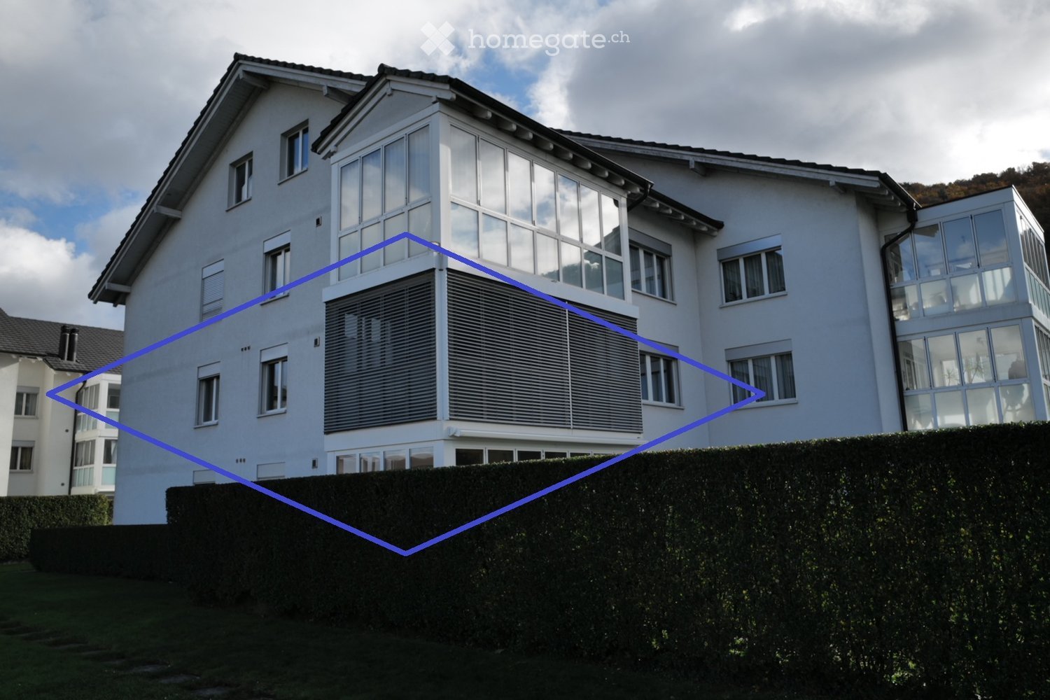 Modern white house, raised ground floor, double glass windows, covered balcony, small hedge