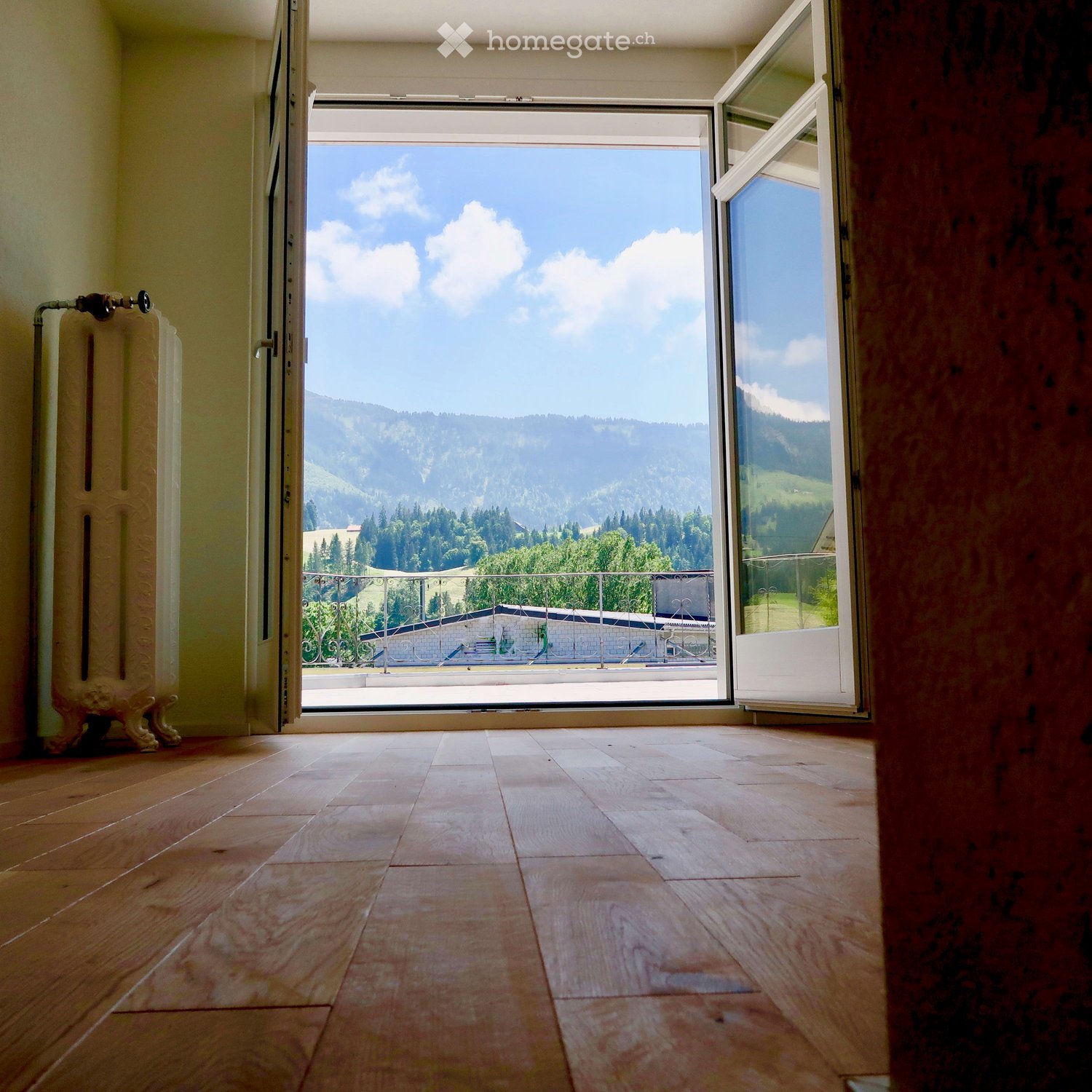 large wooden floor, open sliding glass doors leading to balcony, heater, glass railing on balcony, mountain view, countryside view