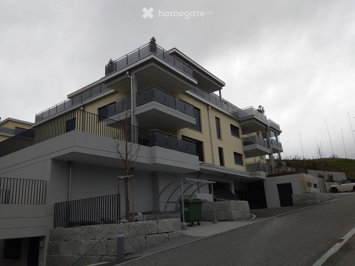 modern apartment building, 4 stories, balconies on each floor, beige and white facade, green tree in front