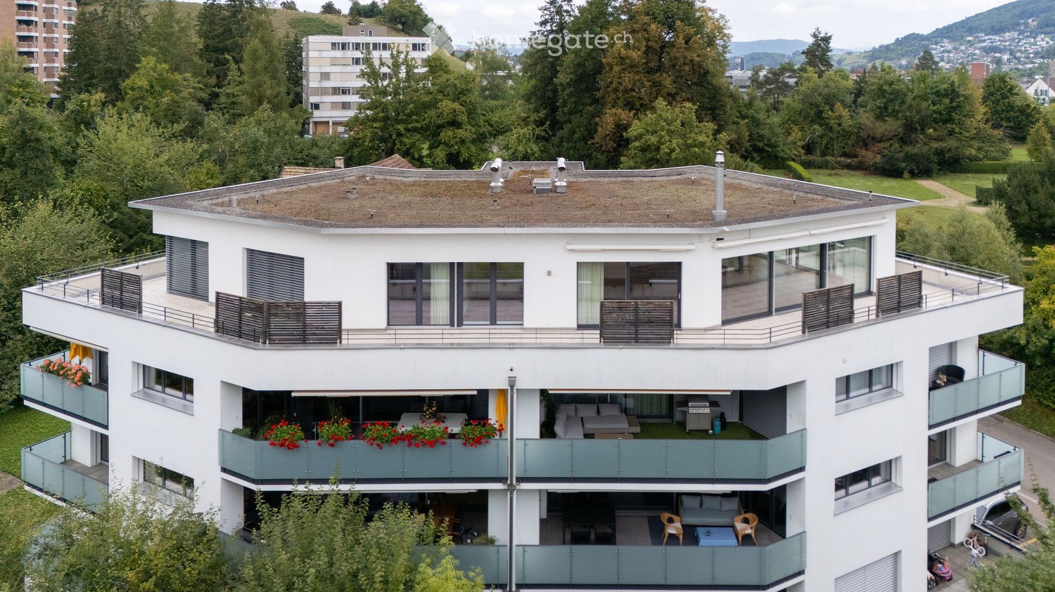 3 story building, white walls, multiple balconies, green lawn, elevated terrace, several plants