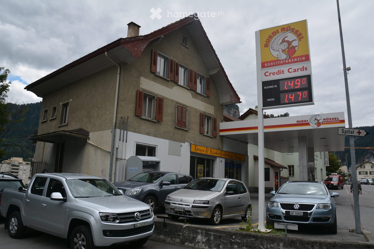 two story building, beige exterior, multiple windows, awnings, red roof, gas station next to it