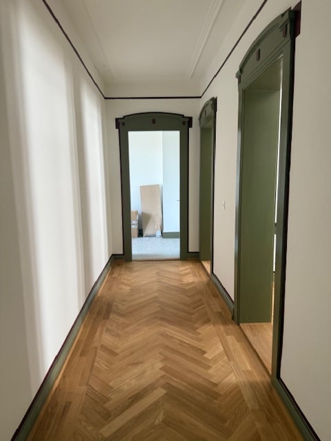 Wooden herringbone parquet flooring, white walls, green doors