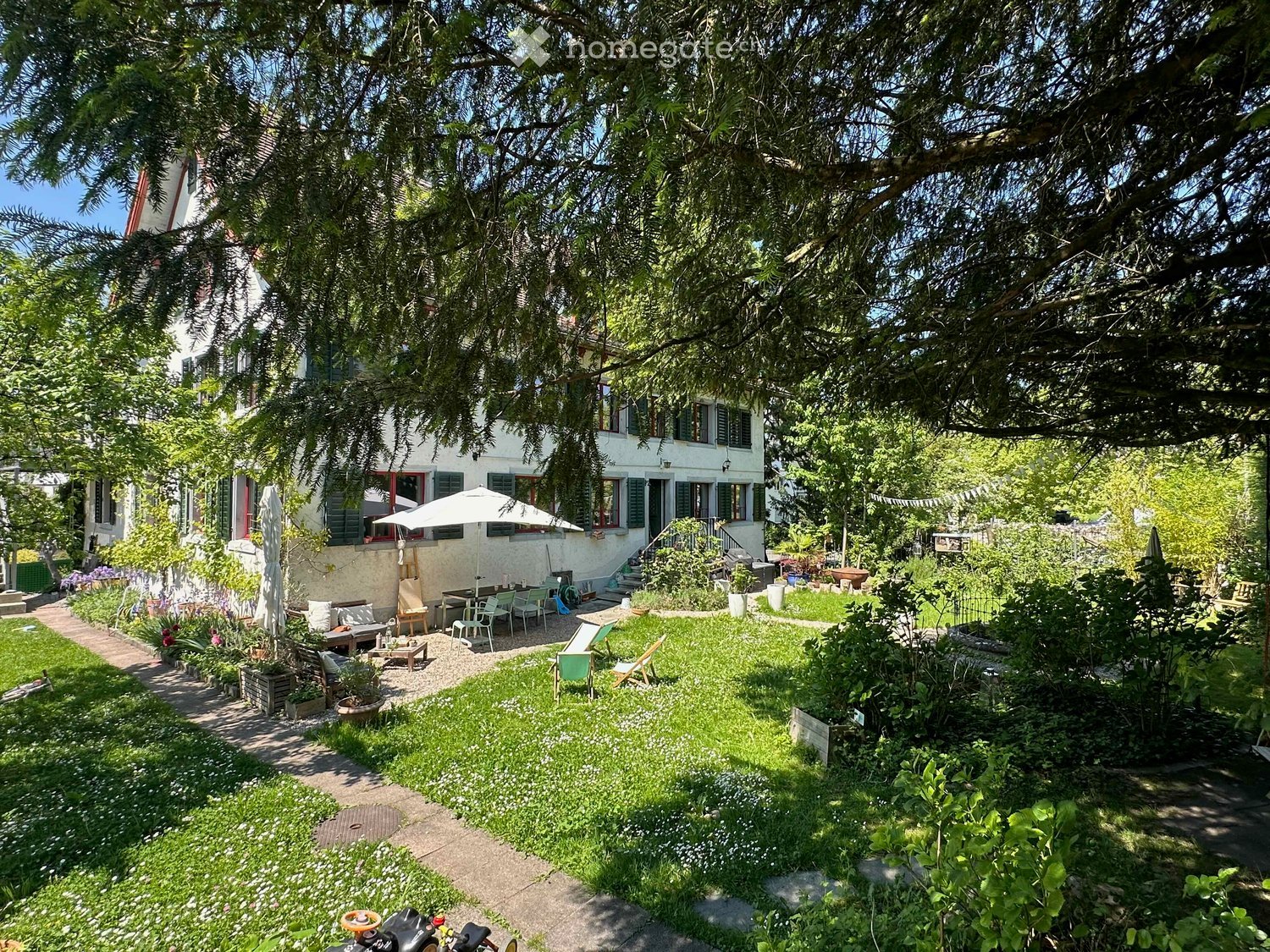 House garden with outdoor seating, table, chairs, potted plants, flowers, well-maintained grass