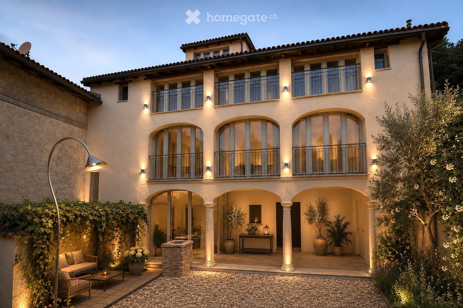 A two-story house with a modern design, featuring arched windows, balconies, and a well-maintained garden area with seating and potted plants.