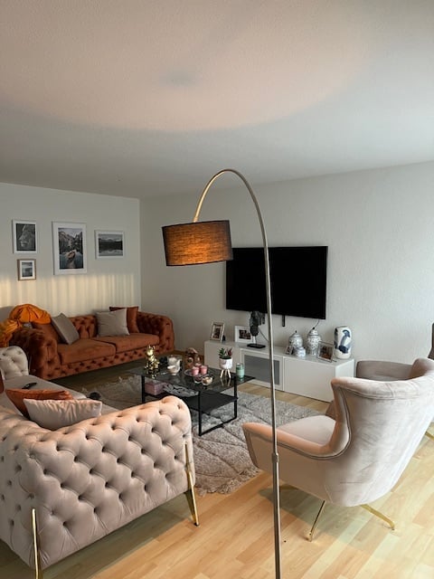 a living room with beige couch, brown couch, TV, floor lamp, coffee table, area rug, wooden floor